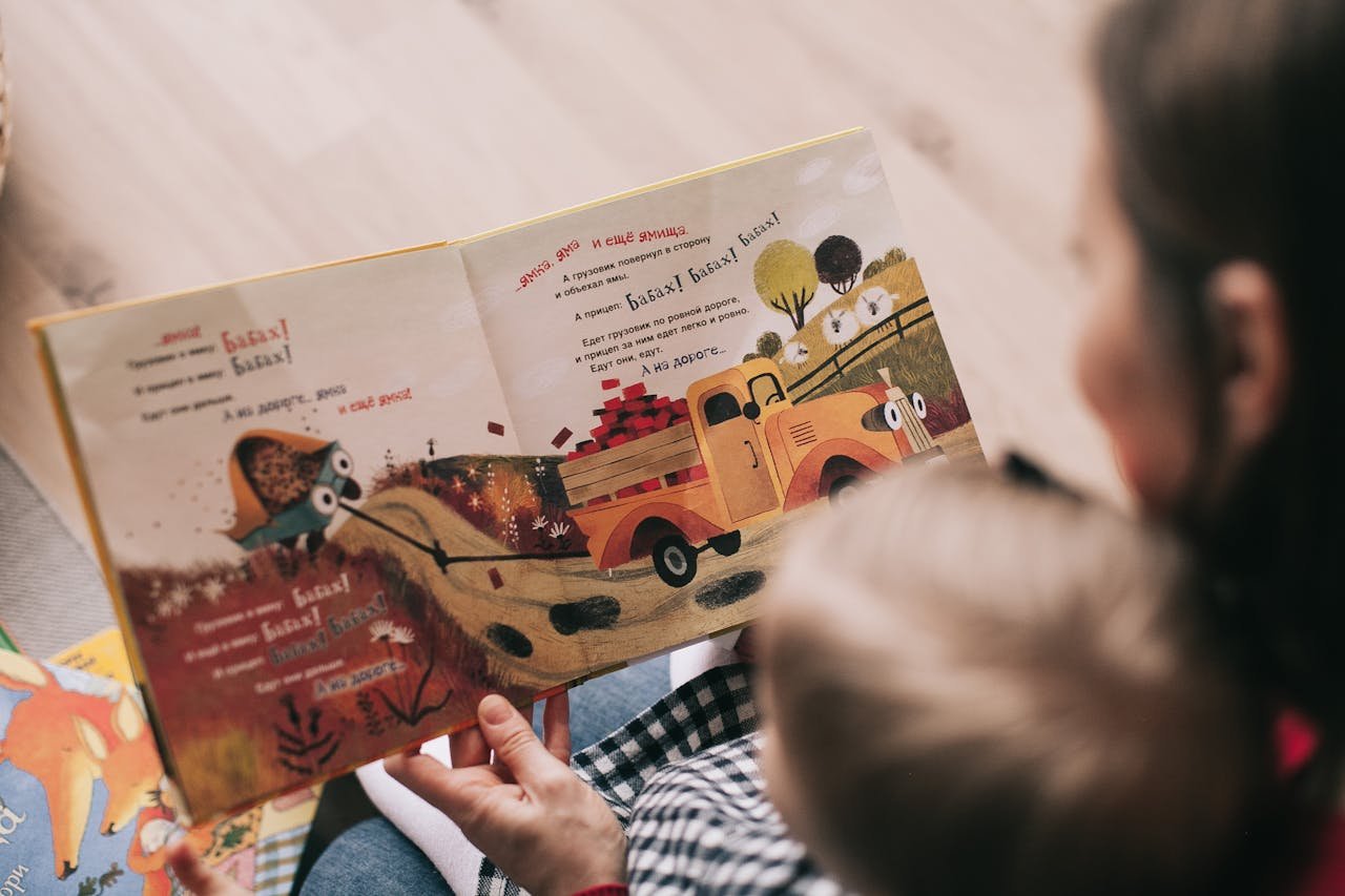 A mother and toddler sharing a story from an illustrated childrens book indoors.
